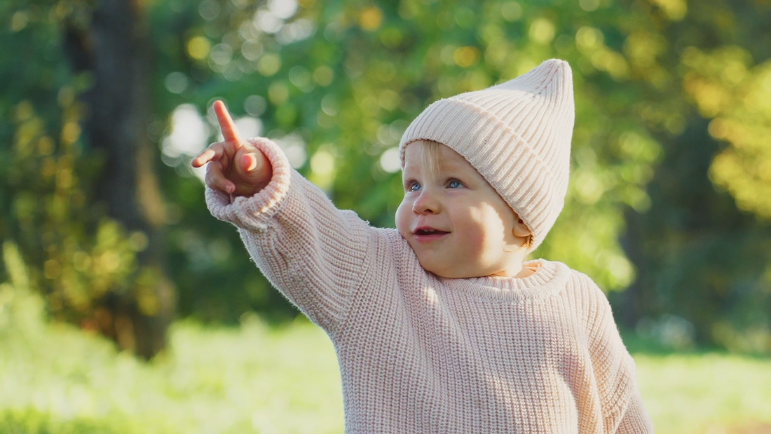 Smiling baby in pink hat and top pointing at the sky, symbolizing natural relief from gas and tummy discomfort