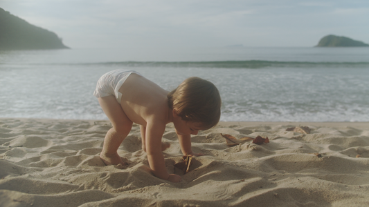 Baby in nappy playing in the sand on an exotic beach with two islands in the background—perfect reason for packing for a stress-free baby holiday