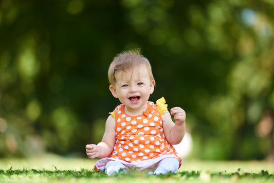A child sat in the great outdoors, holding a flower and giggling