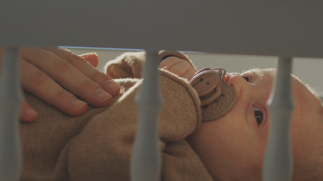 Newborn baby in cot with dummy, comforted by mother’s hand—natural soothing for any child, symbolic of how our nappy balm can calm a baby's mood