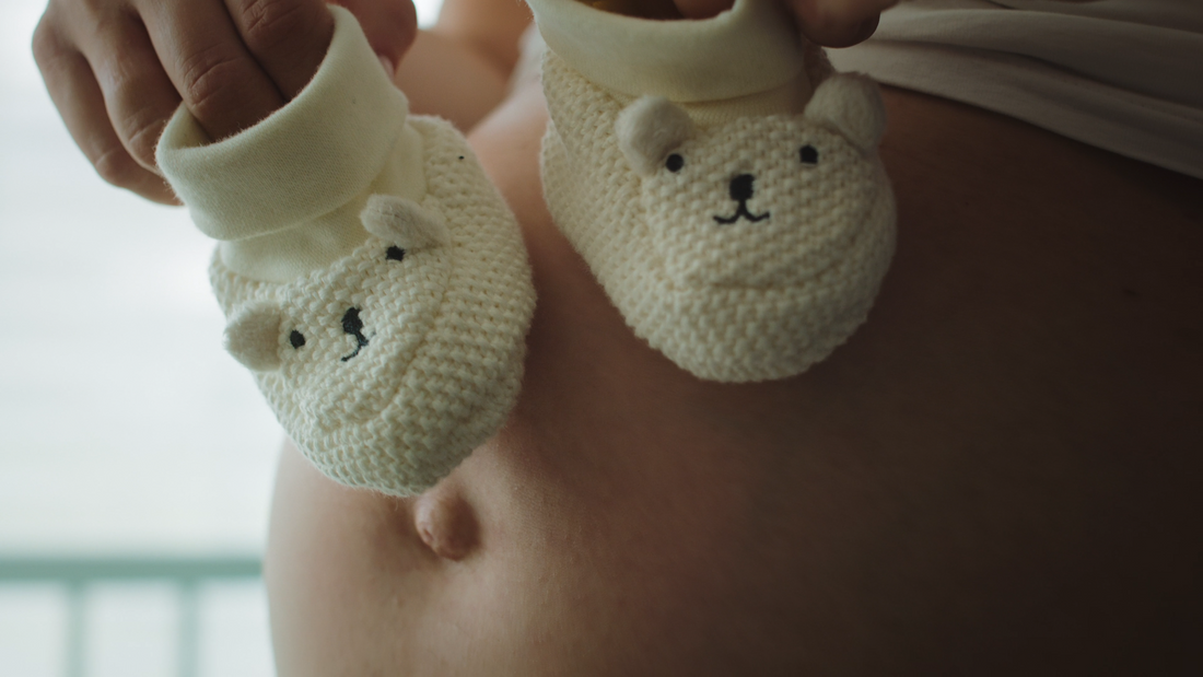Heavily pregnant woman holding two baby shoes, symbolizing thoughtful natural care gift ideas for new mothers